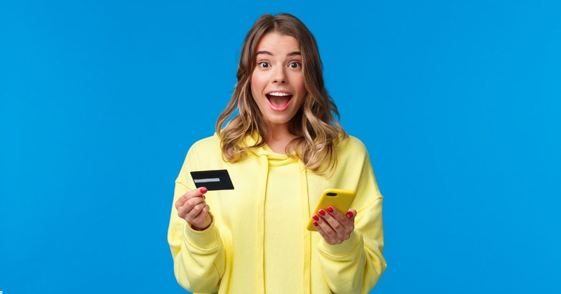 a woman looks surprised while holding a visa card and her phone